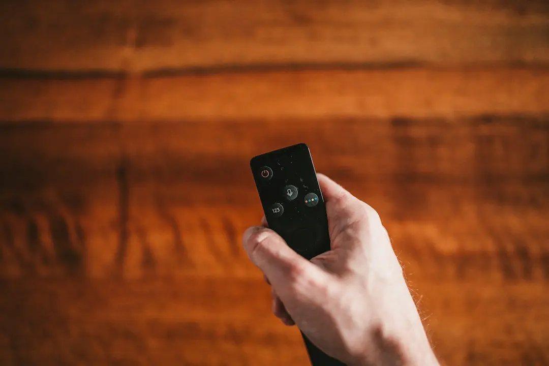 A hand holding a TV remote in front of a television, ready to open an IPTV player for AlwaysTivi